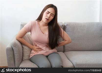 asian woman with menstruation and pain period cramps. young women having painful sitting on sofa at her home