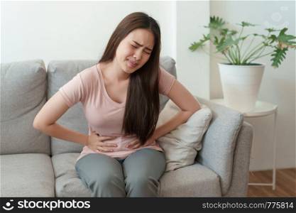 asian woman with menstruation and pain period cramps. young women having painful sitting on sofa at her home