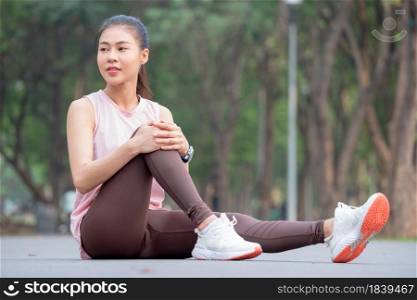 Asian woman with pink sportswear sit with one&rsquo;s knees up and look to her right side on road of park or garden during exercise in the morning.