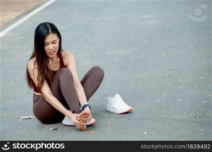 Asian woman with sportswear action of foot pain and sit on road of park or garden during exercise in morning.