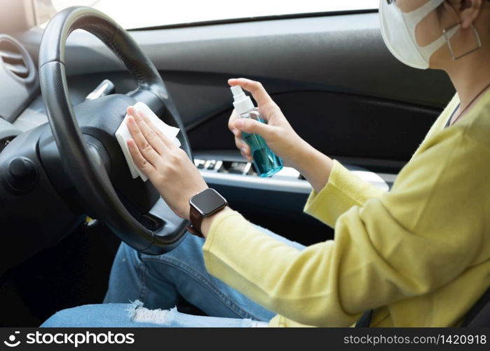 Asian woman with surgical mask spraying alcohol sanitizer on steering wheel for prevent epidemic coronavirus or Coronavirus in her car. Cleaning and disinfection on touching surfaces. Antiseptic, Hygiene, Healthy and Health care concept