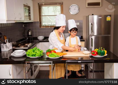 Asian woman young mother with son boy cooking salad food with vegetable holding tomatoes and carrots, bell peppers on plate for happy family cook food enjoyment lifestyle kitchen in home