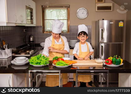 Asian woman young mother with son boy cooking salad food with vegetable holding tomatoes and carrots, bell peppers on plate for happy family cook food enjoyment lifestyle kitchen in home