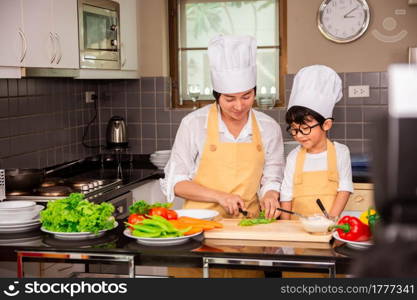 Asian woman young mother with son boy cooking salad food with vegetable holding tomatoes and carrots, bell peppers on plate for happy family cook food enjoyment lifestyle kitchen in home