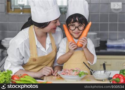 Asian woman young mother with son boy cooking salad food with vegetable holding two carrots and tomatoes, bell peppers for happy family cook food enjoyment lifestyle kitchen