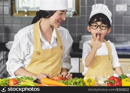 Asian woman young mother with son boy cooking salad food with vegetable holding two tomatoes and carrots, bell peppers for happy family cook food enjoyment lifestyle kitchen