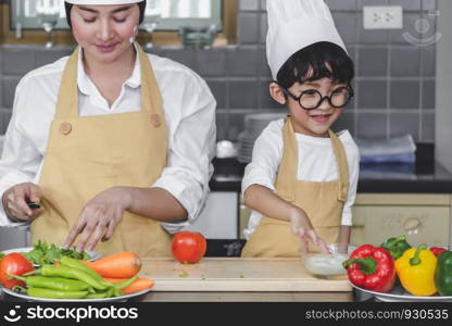 Asian woman young mother with son boy cooking salad mom sliced vegetables food son tasting salad dressing with vegetable carrots and tomatoes, bell peppers for happy family cook food enjoyment lifestyle kitchen