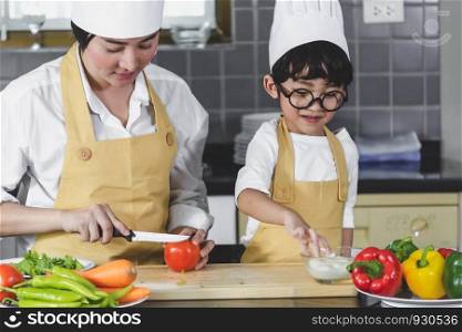 Asian woman young mother with son boy cooking salad mom sliced vegetables food son tasting salad dressing with vegetable carrots and tomatoes, bell peppers for happy family cook food enjoyment lifestyle kitchen