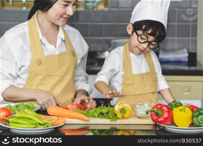 Asian woman young mother with son boy cooking salad mom sliced vegetables food son tasting salad dressing with vegetable carrots and tomatoes, bell peppers for happy family cook food enjoyment lifestyle kitchen