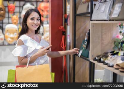 Asian women and Beautiful girl is holding shopping bags and using a smart phone and smiling while doing shopping in the supermarket/mall