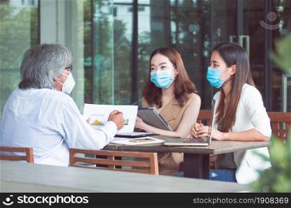 Asian women and boss wearing masks, keeping social distancing and working together