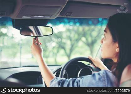 Asian women are adjusting the rearview mirror of the car