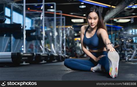 Asian women are sitting stretching their legs to stretch their muscles to warm up or cool down after a workout at fitness or gym with a patition barrier for social distancing in sport healthy concept