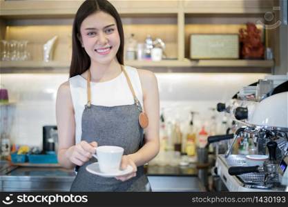 Asian women Barista smiling and holding coffee cup and using machine in coffee shop counter - Working woman small business owner food and drink cafe concept