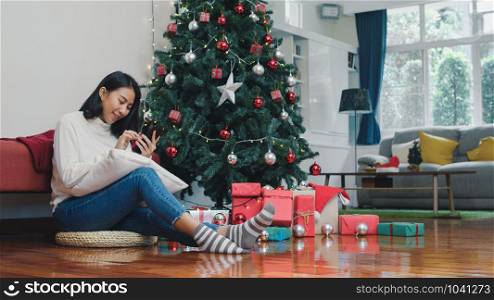 Asian women celebrate Christmas festival. Female teen relax happy using smartphone check social media enjoy xmas winter holidays in living room at home.