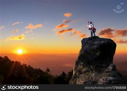 Asian women climbers or backpackers are standing, looking out through the tall treetops on the rocky peaks at sunset, success and winner, leader concept.. Leader on top.