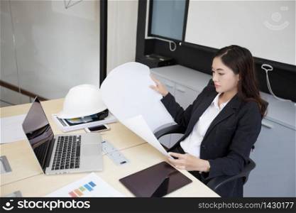 Asian women engineering holding blueprints and have hard hat on table for working at office