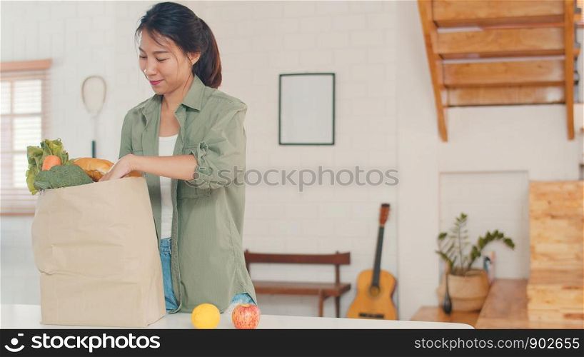 Asian women holding grocery shopping paper bags at home, young Asia girl happy buy vegetables and fruit healthy and organic product from supermarket put it in kitchen in the morning concept.