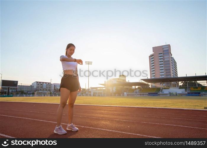 Asian women is watching the sport watch or smart watch for jogging on stadium track -healthy lifestyle and sport concepts