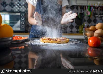 Asian women preparing a pizza, knead the dough and puts ingredients on kitchen table