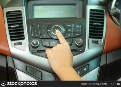 Asian Women press button on car radio for listening to music.