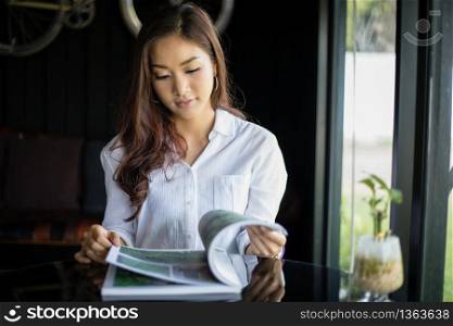 Asian women smiling and reading a book for relaxation at coffee shop
