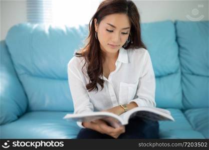 Asian women smiling and reading a book for relaxation at home