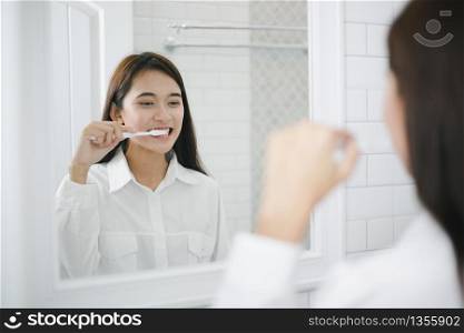 Asian women squeezing toothpaste and brushing their teeth in the bathroom in the morning.