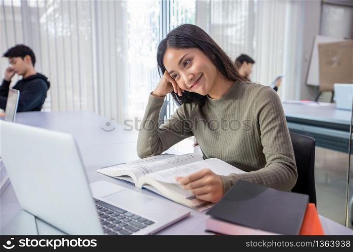 Asian women Students Smile and reading book and using notebook for helps to share ideas in the work and project. And also review the book before the exam
