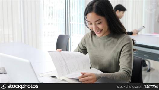 Asian women Students Smile and reading book and using notebook for helps to share ideas in the work and project. And also review the book before the exam