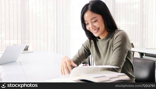 Asian women Students Smile and reading book and using notebook for helps to share ideas in the work and project. And also review the book before the exam