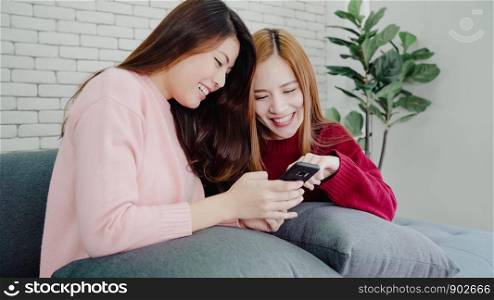Asian women using smartphone checking social media in living room at home, group of roommate friend enjoy funny moment while lying on the sofa. Lifestyle women relax at home concept.