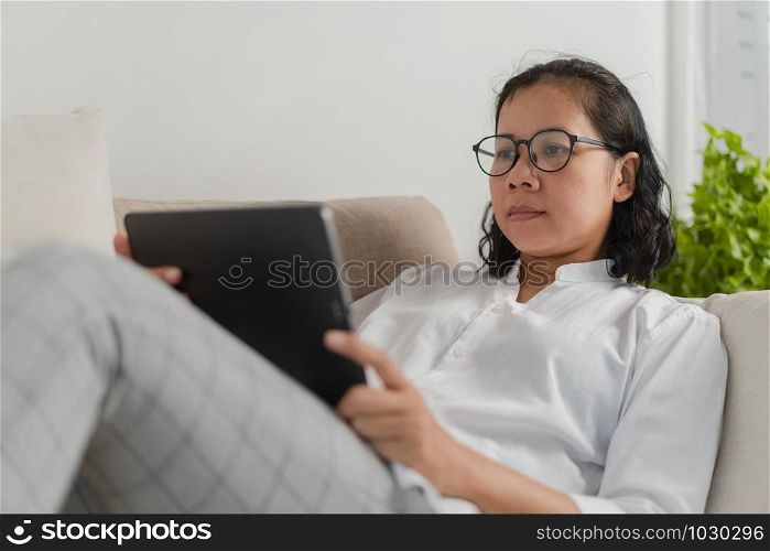 Asian women wear glasses using tablet while sitting work on the sofa at home.