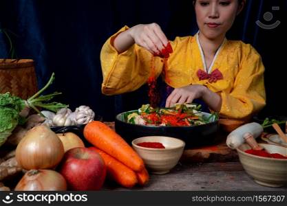 Asian women wearing Korean traditional costumes (hanbok) are mixing fresh stir-fry and kimchi ingredients with ingredients such as salt, garlic, gochugaru, fresh vegetables.