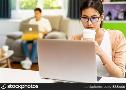 Asian working woman use computer notebook laptop with delivery coffee cup work from home in living room with social distance to couple in background while city lockdown. Work at home concept.