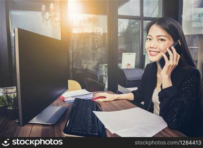 asian working woman using computer in home office and talking on mobile phone with happiness face