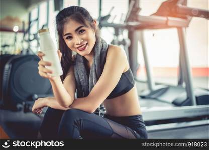 Asian workout woman showing milk bottle during break or relax. Food drinks and Healthy concept. Fitness gym and equipment theme