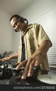 Asian young adult male DJ standing with hand on spinning record on turntable and smiling.
