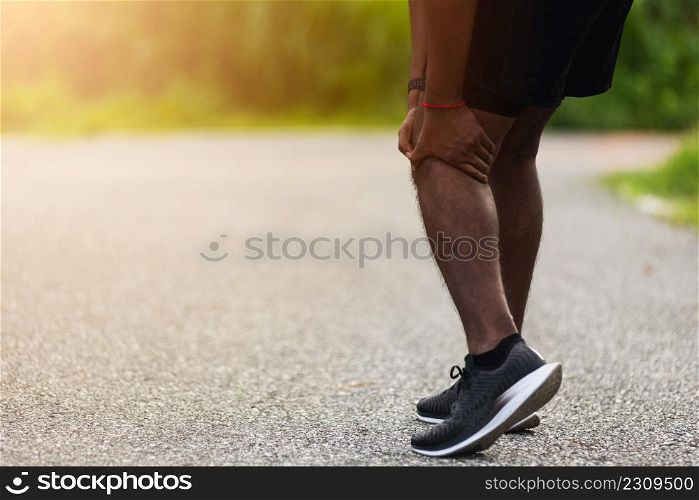 Asian young athlete sport runner black man stand wear feet shoe active running training at outdoor he use hands hold on his knee pain while running, healthy exercise injury osteoarthritis from workout