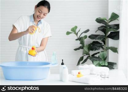Asian young beautiful mother wear bathrobe is having fun with prepare equipment for bathing her newborn baby at home. Child care bathing concept