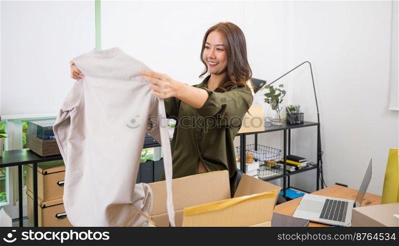 Asian young beautiful woman unboxing cardboard delivery package and holding with ordered clothes, Excited lady shopper unpack cardboard box with clothes, happy and smiling
