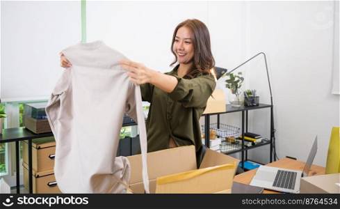 Asian young beautiful woman unboxing cardboard delivery package and holding with ordered clothes, Excited lady shopper unpack cardboard box with clothes, happy and smiling