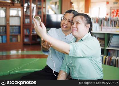 Asian young blind woman disabled person taking selfie using smart phone with her senior colleague woman in creative workplace