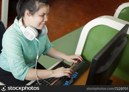 Asian young blind woman with headphone using computer with refreshable braille display or braille terminal a technology device for persons with visual disabilities.