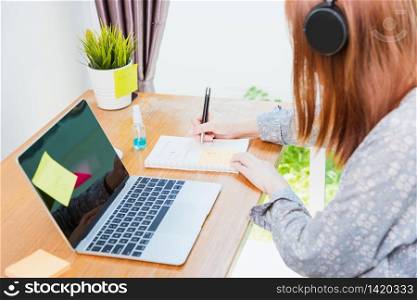 Asian young business woman wearing face mask protective working from home office with laptop computer he quarantines disease coronavirus or COVID-19 and write note booklist work today