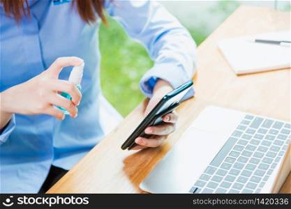 Asian young business woman wearing face mask protective working from home office with laptop computer he quarantines disease coronavirus or COVID-19 using sprays sanitizer cleaning smart mobile phone