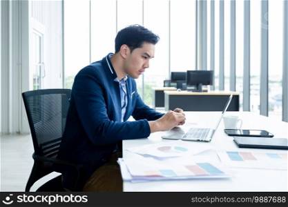 asian young businessman see a successful business plan on the laptop computer and pen on wooden table background in office,business expressed confidence embolden