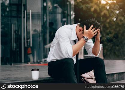 Asian young businessman stress sitting in front office with his hands covering his head against.
