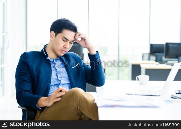 Asian young businessman worked late and tired fell asleep or having stressful time on laptop computer In the office room background.