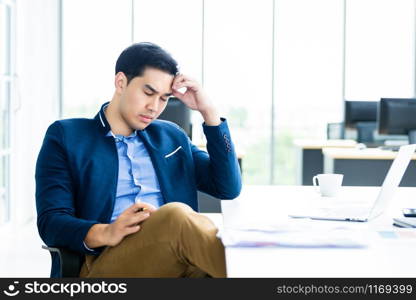 Asian young businessman worked late and tired fell asleep or having stressful time on laptop computer In the office room background.